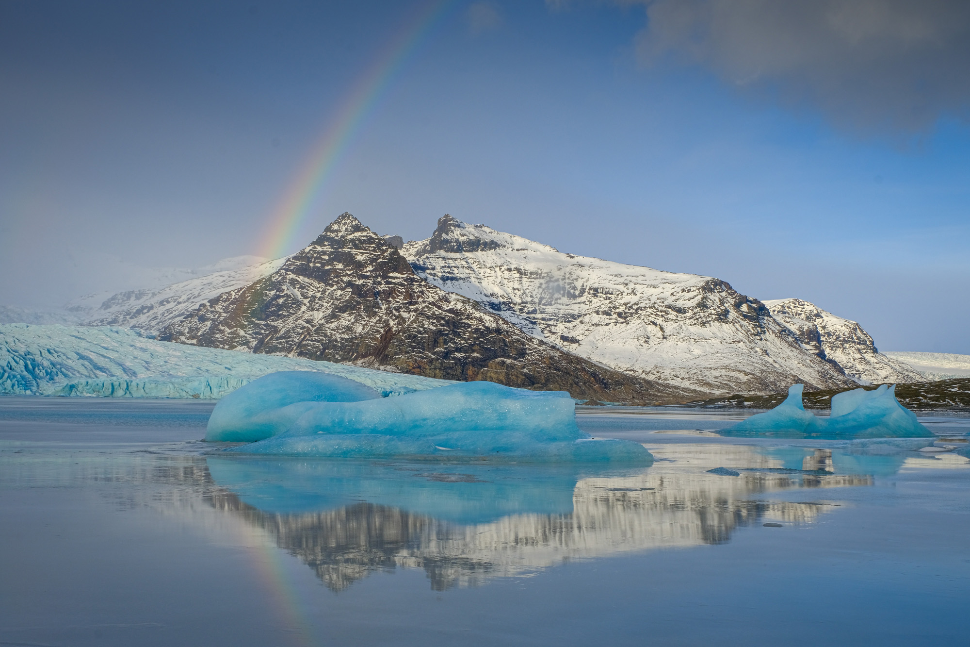 icebergs and mountains around lagoon with rainbow in Iceland