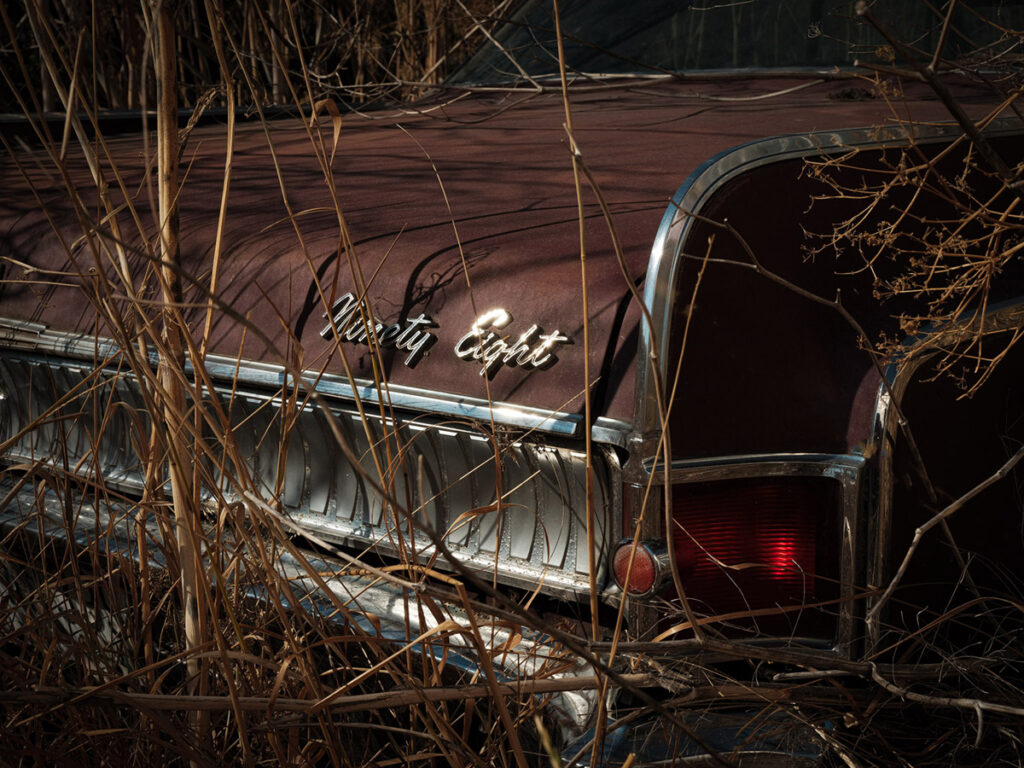 An old car sits abandoned in the weeds