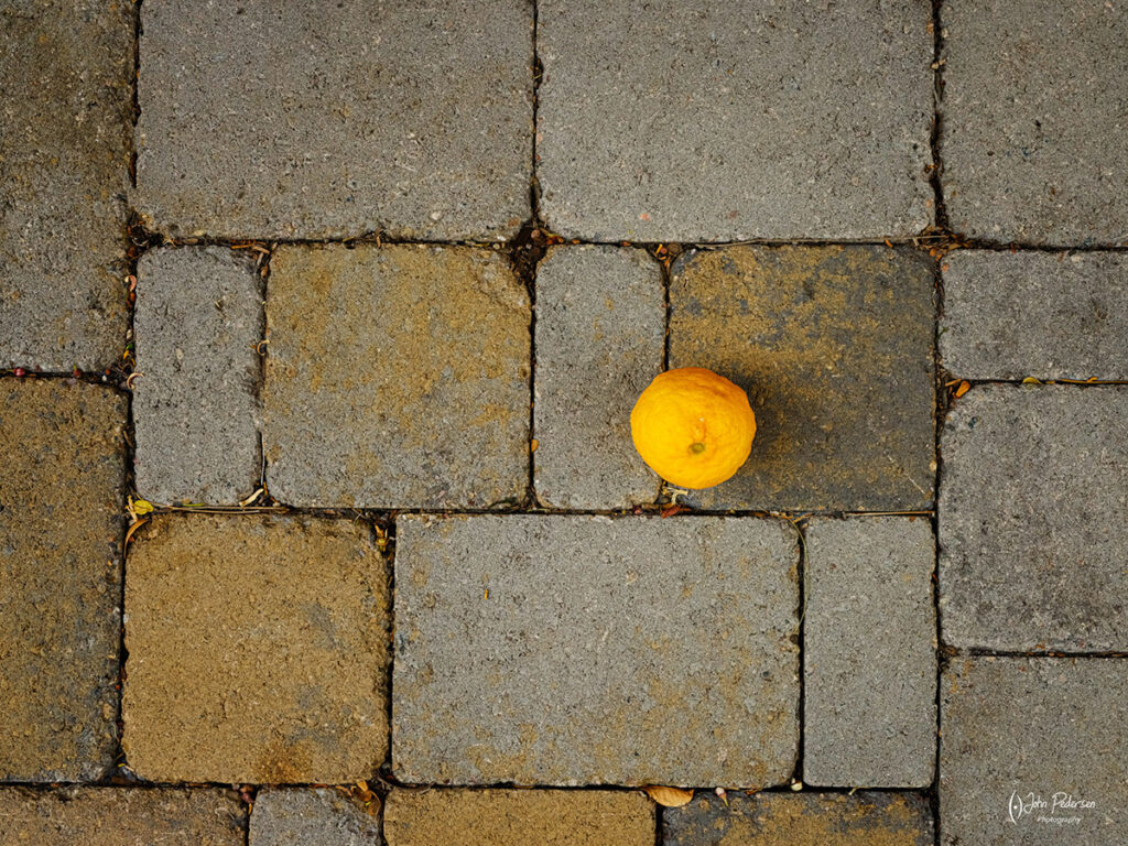 A lemon rests on a brick sidewalk