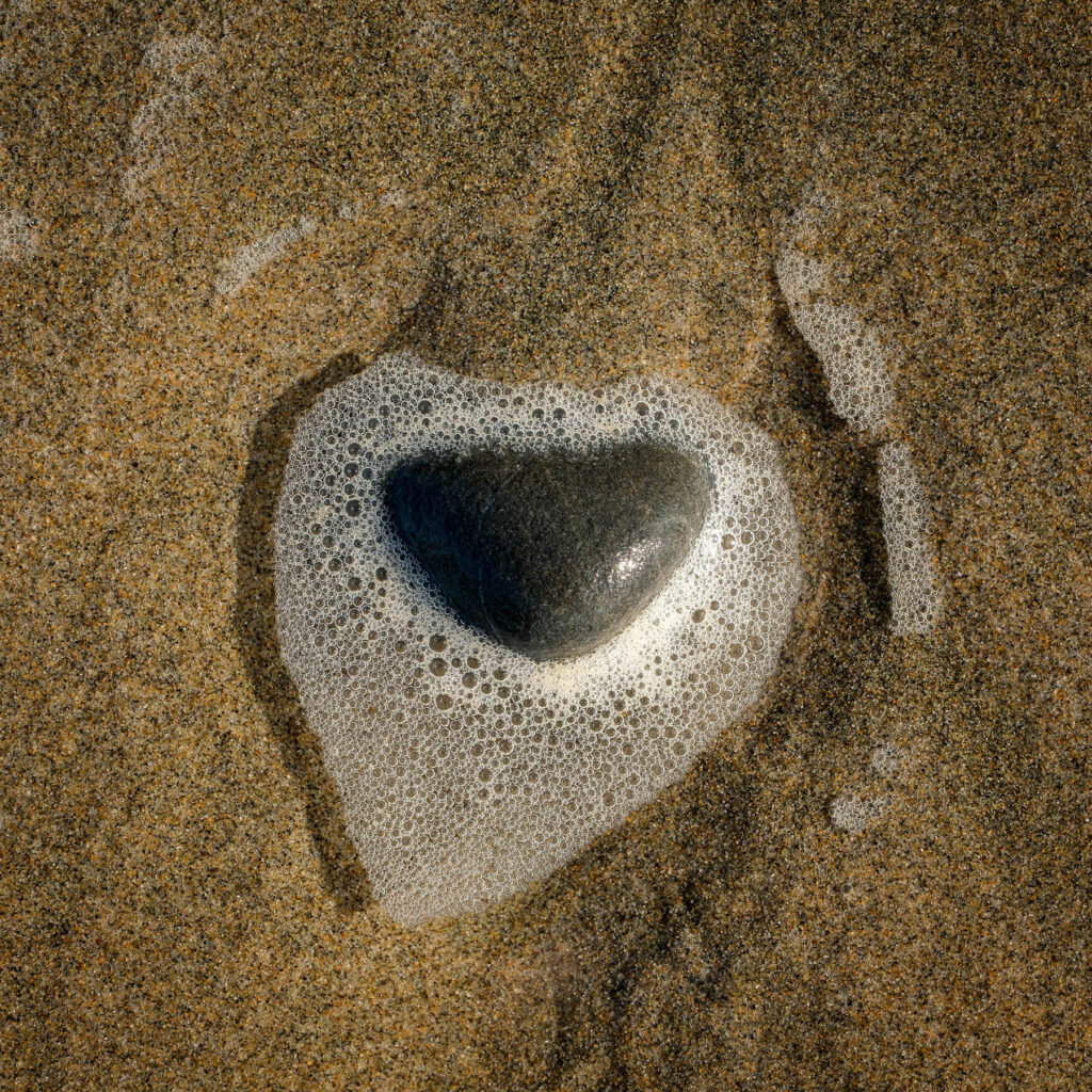 A rock and sea foam shaped like a heart on the beach in Oregon