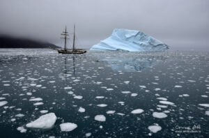 Iceberg and sailing ship in fjord of Greenland