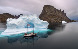 Iceberg in calm water with sailing ship in Greenland