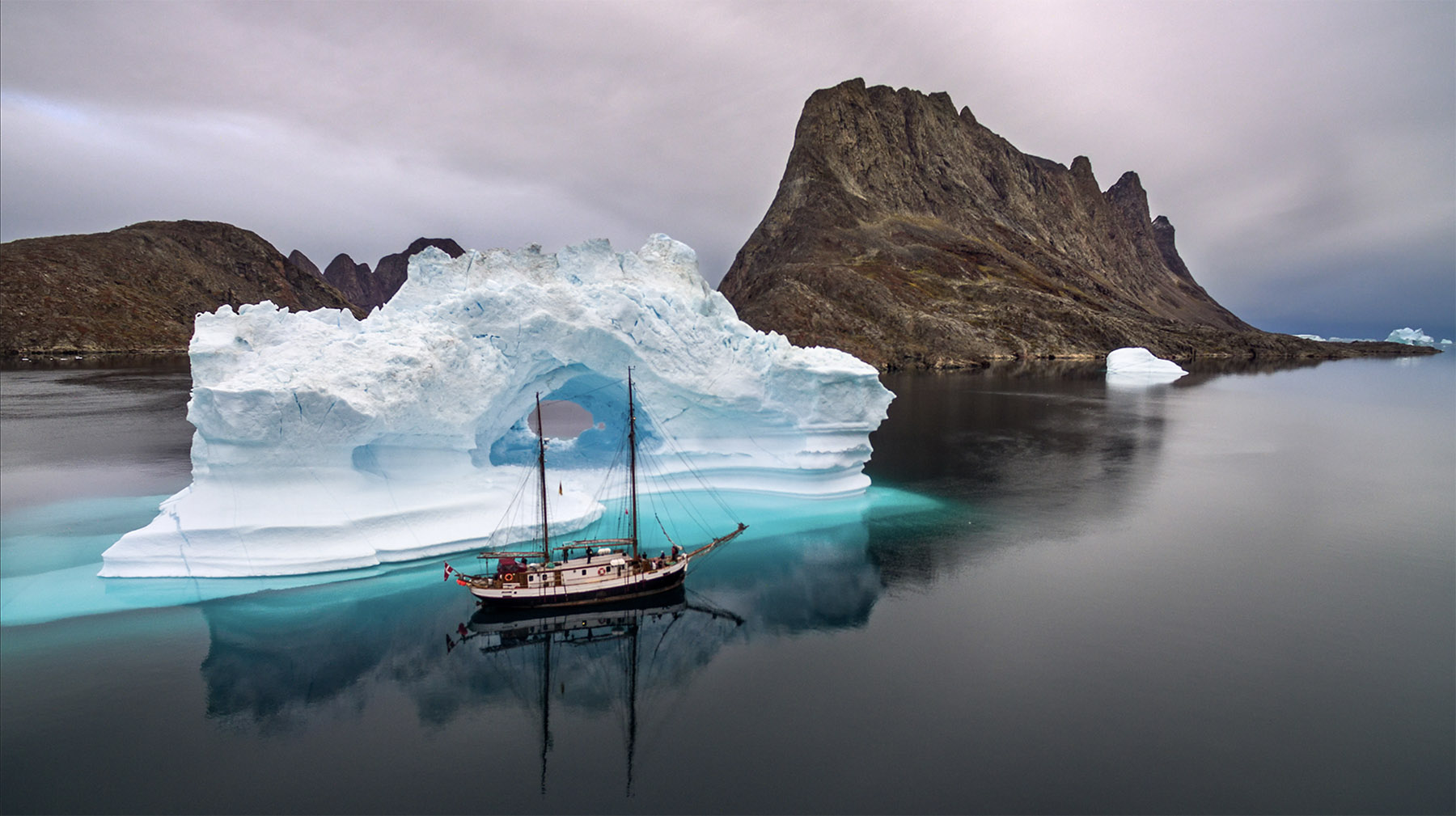 Iceberg in calm water with sailing ship in Greenland