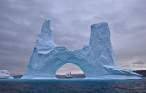 A sailing ship seen between an arch in an iceberg in Greenland