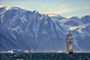A sailing ship with snowcapped mountains in the background